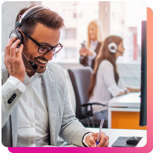 Busy call center Male call center agent smiling while talking on a headset while wielding a pen